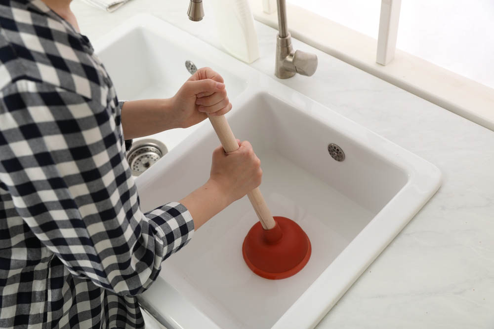 person using a plunger on a clogged drain
